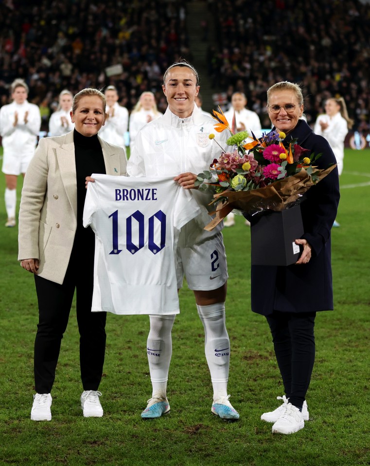 Lucy Bronze comemorando sua 100ª aparição na Inglaterra ao lado de Kay Cossington (à esquerda) e Sarina Wiegman em 16 de fevereiro de 2023