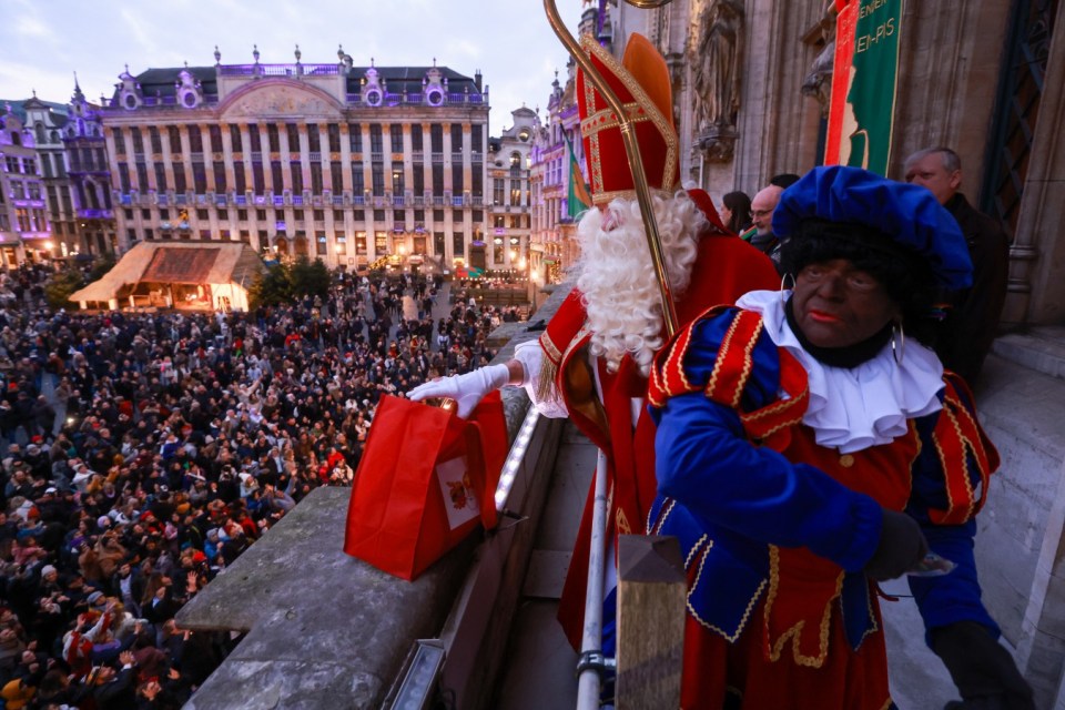 Uma pessoa vestida como Zwarten Piet com blackface cumprimenta os espectadores em um evento de Natal