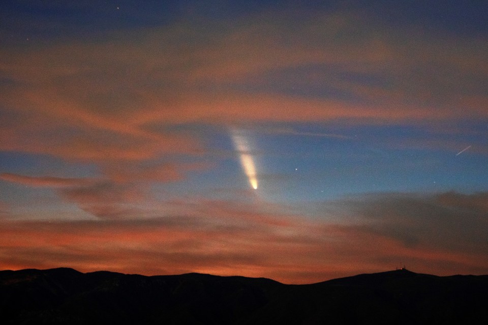 um cometa é visível no céu noturno acima das montanhas