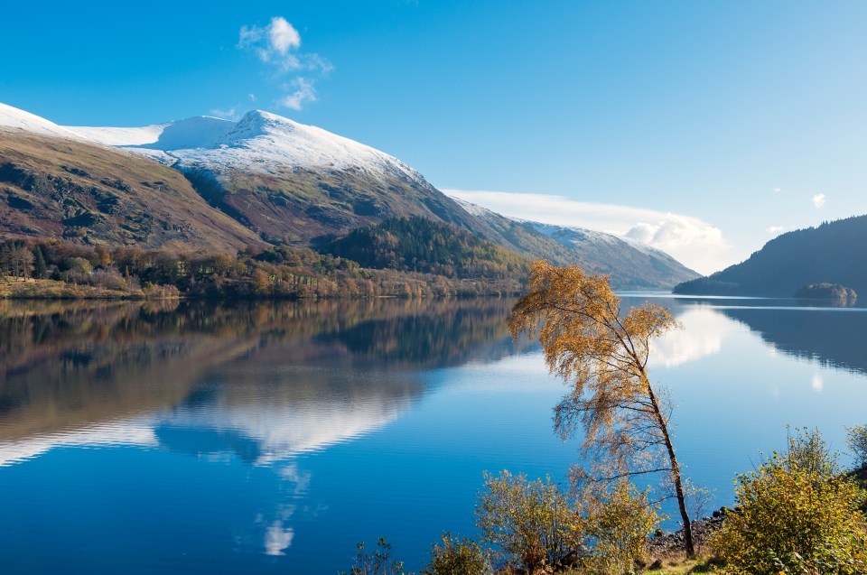 Montanha Helvellyn coberta de neve refletida em um lago calmo.