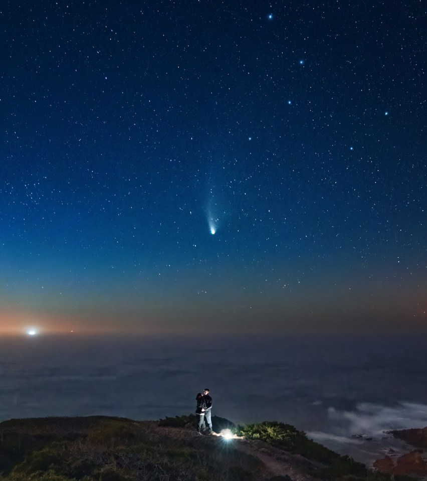 um casal parado no topo de uma colina sob um céu noturno estrelado