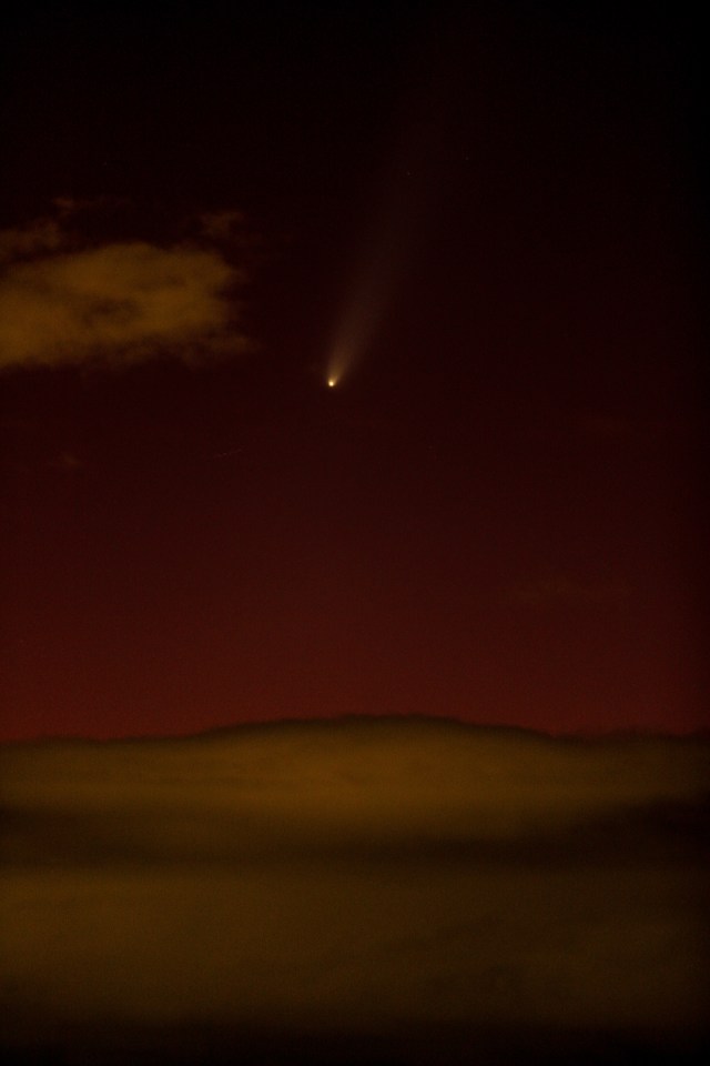 um cometa é visível no céu noturno acima de um deserto