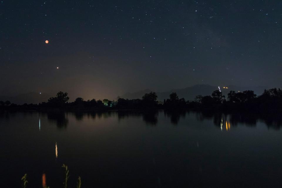 Lua de sangue e Marte refletidos em um lago à noite.